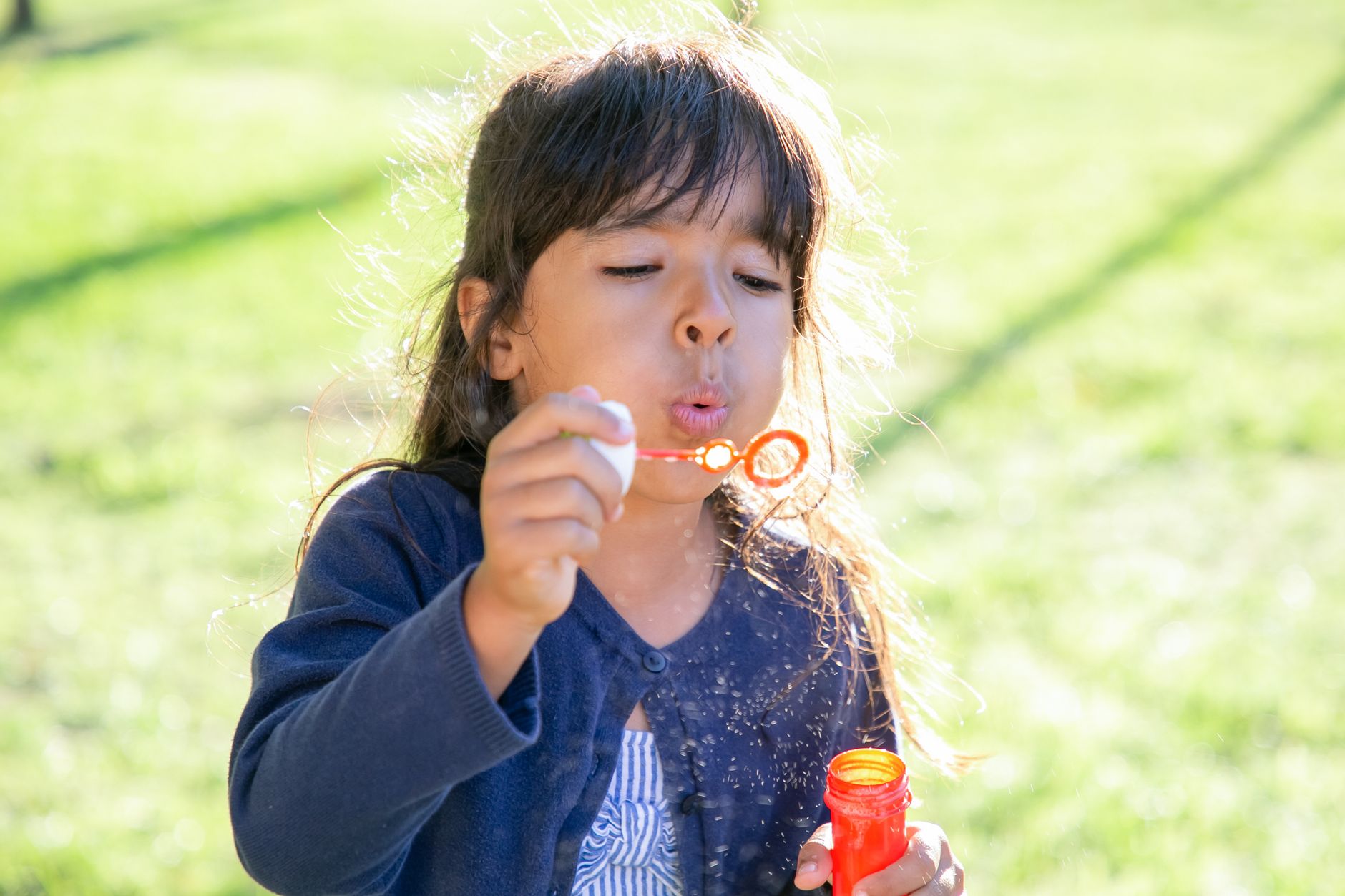Fillette qui joue avec un tube de bulles de savon au parc