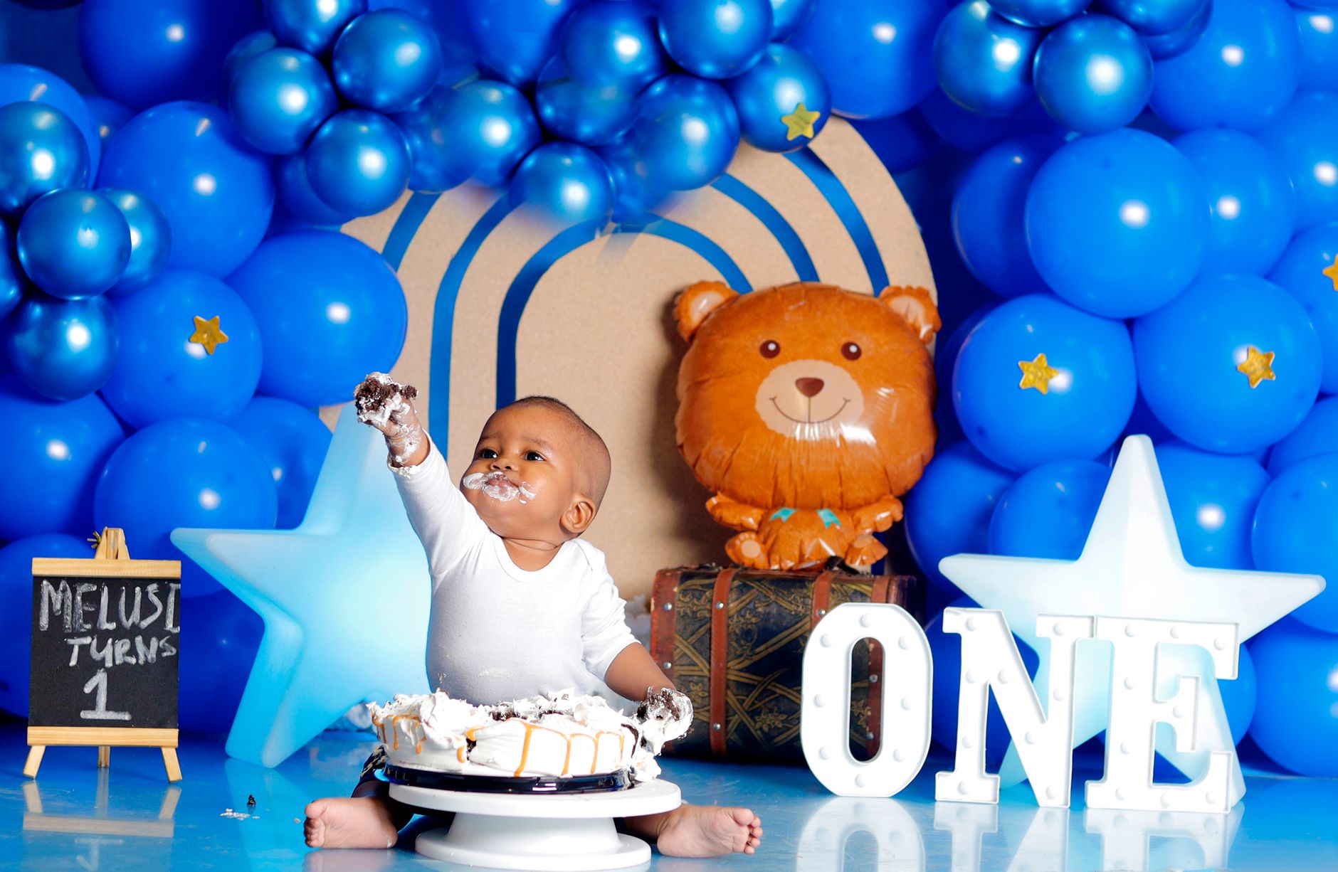 Bébé devant son gâteau entouré de ballons bleus